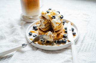 pancakes on a white plate drizzled with yoghurt, blueberries and honey