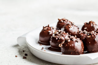 Chocolate covered protein balls topped with nuts on a white plate and on a white background 