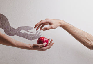 One hand holding an apple and another taking it with the shadow of a claw