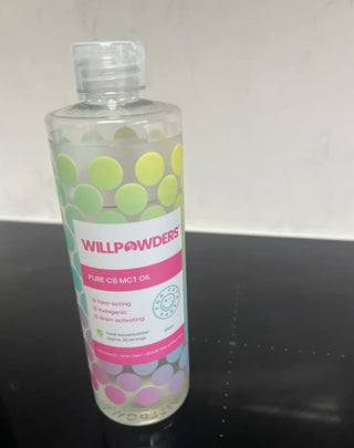 A bottle of WillPowders C8 MCT Oil, on a black surface against a white wall