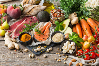 A spread of healthy foods including fruits, vegetables, raw salmon and beef, bread, various nuts on a wooden surface.